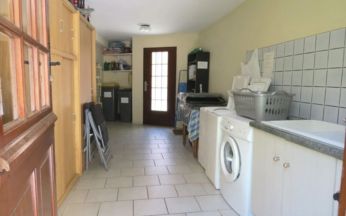 Lavadero con lavadora, fregadero, armarios y cubos de reciclaje